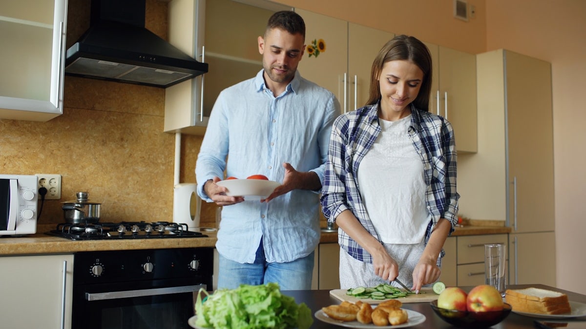 Happy young couple embracing and talking in the kitchen while cooking breakfast at home in the morning